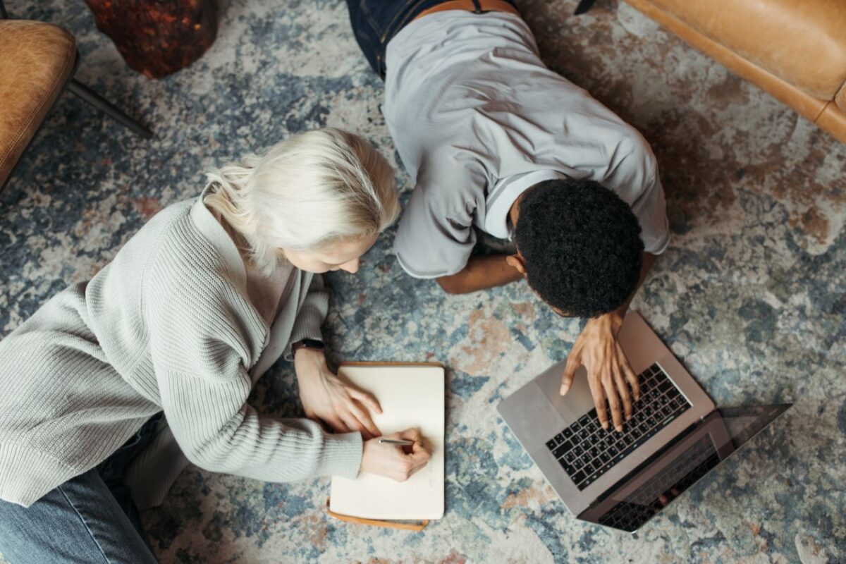 Offres Two adults working together on the floor with a laptop and notebook.