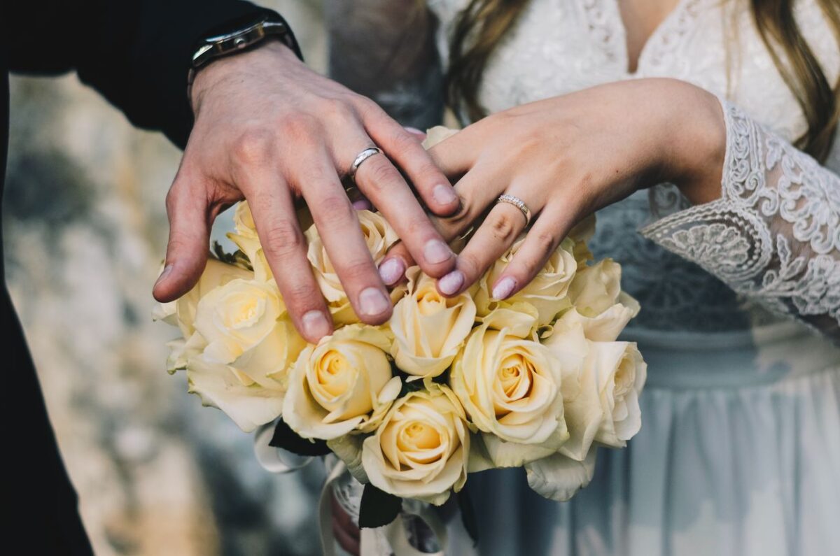 Ma Vidéo de Mariage Close-up of a couple's hands displaying wedding rings above a bouquet of yellow roses.