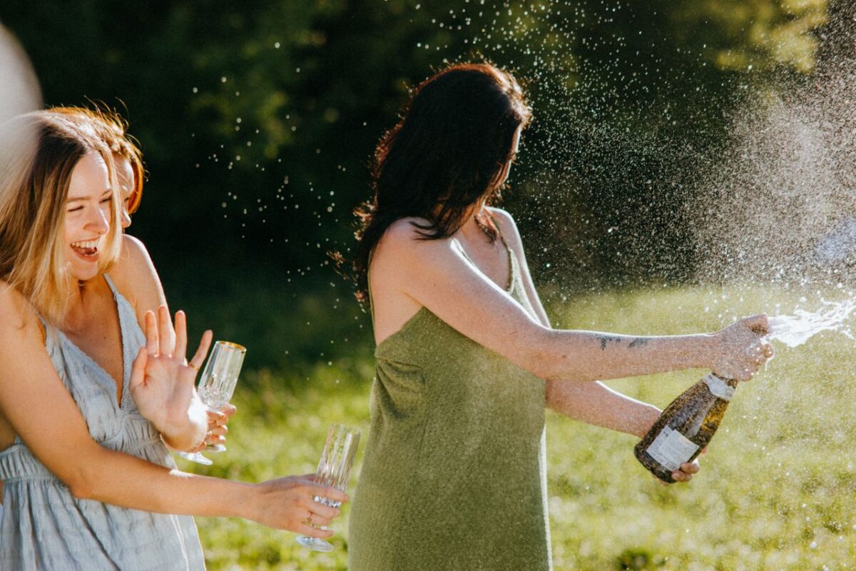 Offres Joyful women celebrating with champagne in a sunny outdoor setting.